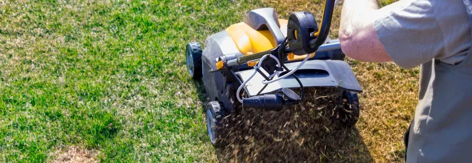 Person vertikutiert Rasen